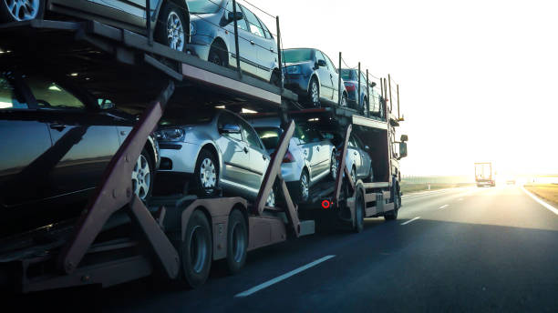 A FL Auto Transport Naples, FL car carrier truck transports multiple new vehicles on a highway during daylight, heading towards the horizon.