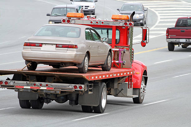Tilt bed tow truck transporting a broken down vehicle to a service facility. Shallow dof with focus on trucks cab, slight motion blur.
