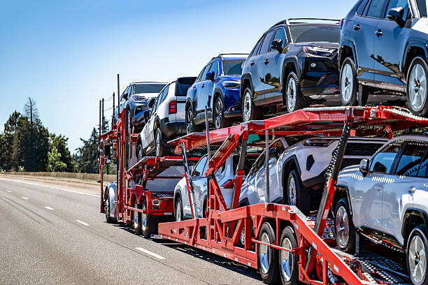 Big rig white car hauler semi truck with extended cab for truck driver rest truck transporting cars and crossovers on two level modular semi trailer running on the wide highway road